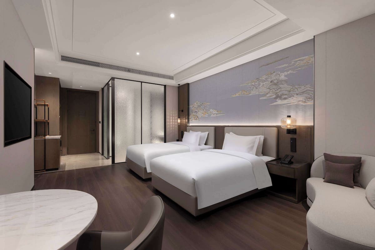 A modern hotel room with two beds, a dining table, and a large artwork on the wall.