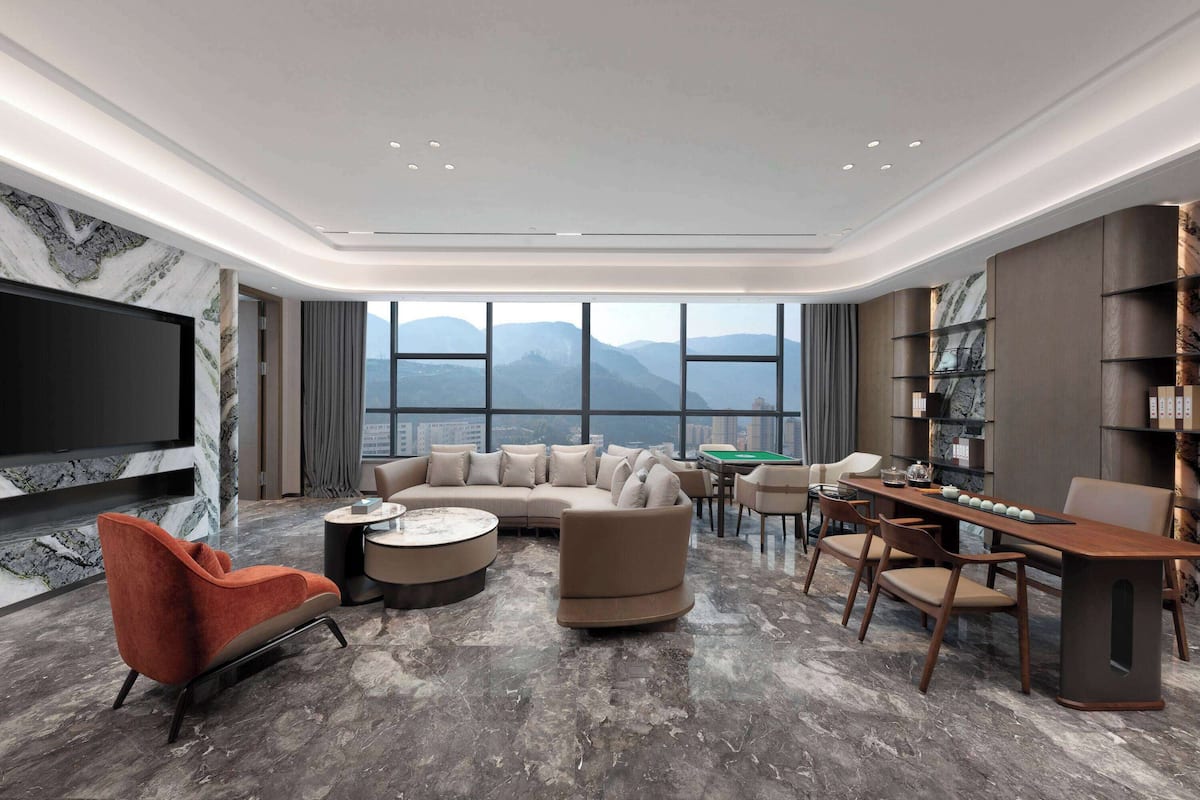 A modern living room with a large flat-screen TV, a sectional sofa, a red armchair, a coffee table, and a dining area with a wooden table and chairs.