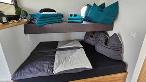 Ein Etagenbett mit Ablagefläche darüber, voll mit gefalteten Handtüchern und Kissen.