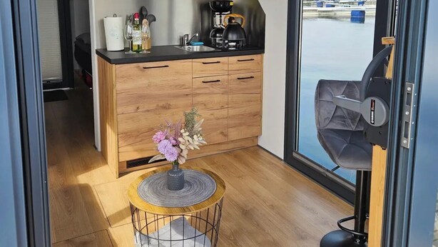 Eine moderne Küche mit Holzausstattung, einer Kaffeemaschine und Blick auf Boote durch ein großes Fenster.