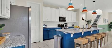 A modern kitchen with white cabinets, a blue island, and a stainless steel refrigerator.