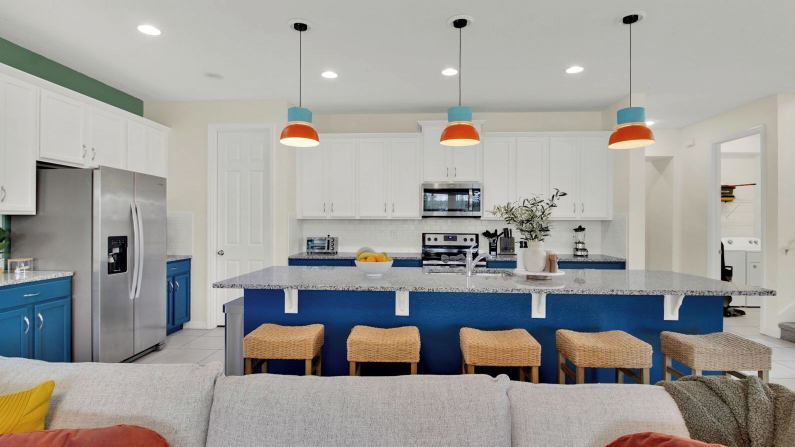 A modern kitchen with white cabinets, a large island with bar stools, stainless steel appliances, and pendant lighting.