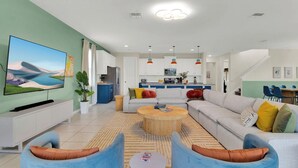 A modern living room with a flat-screen TV, sofas, a coffee table, and a kitchen in the background. - Sleeps 20! 9bdr, Star Wars-themed Game Room, Pool, Hot Tub Nassau by Avantstay (Kissimmee)