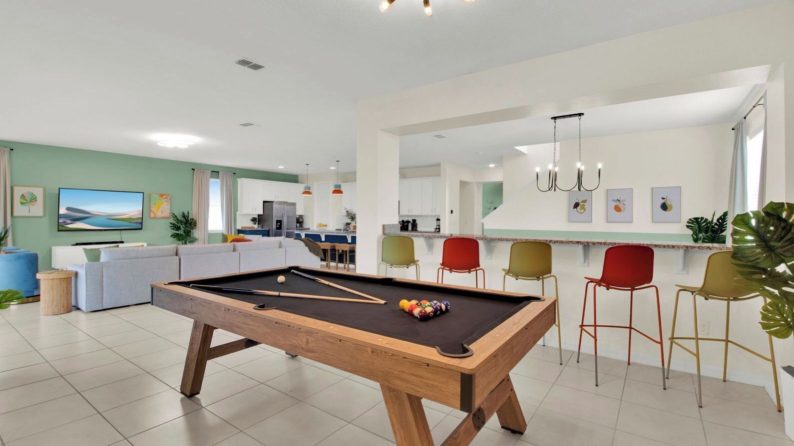 Een moderne woonkamer met een pooltafel, een bank en een eethoek met kleurrijke stoelen.