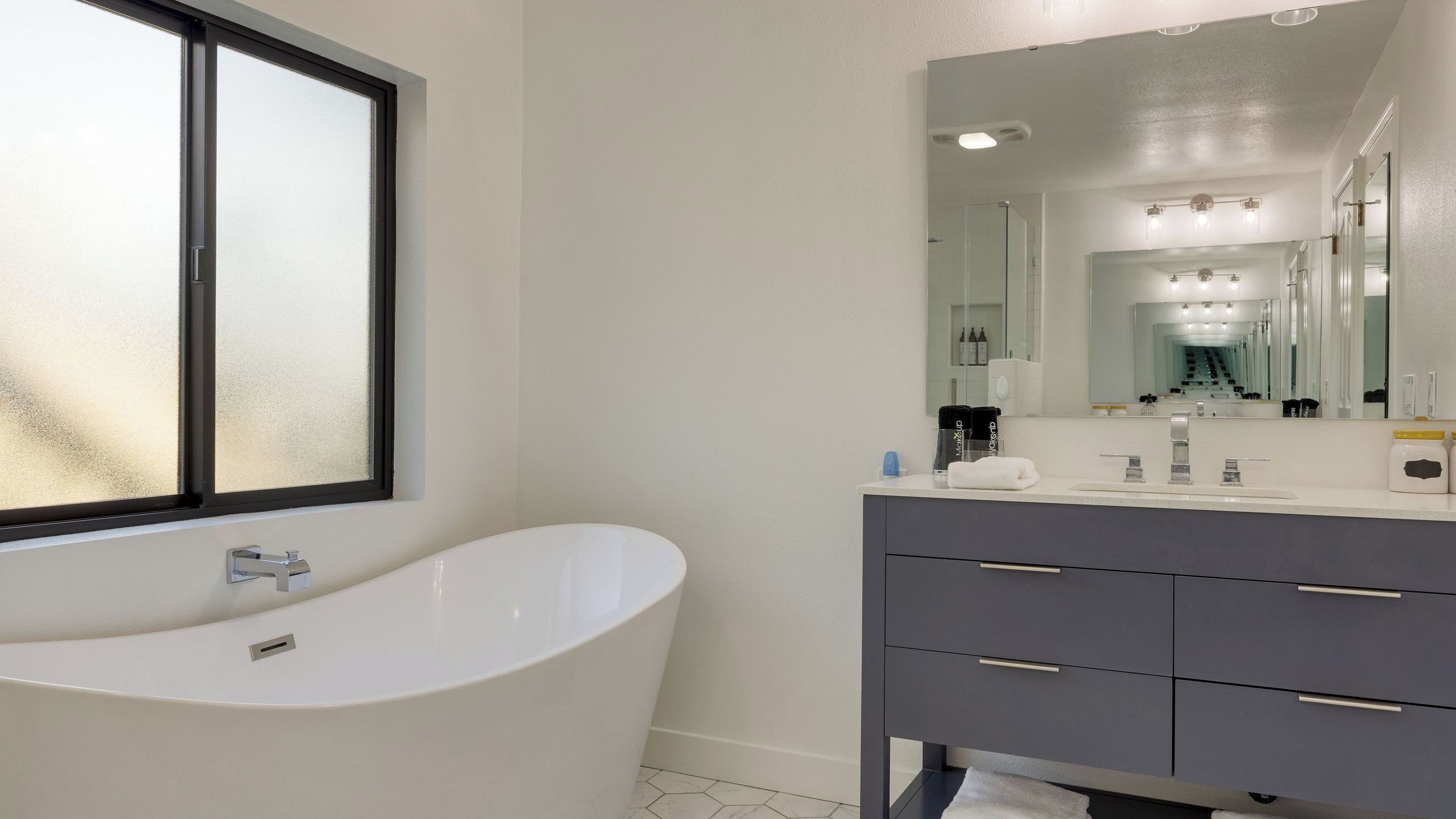 A modern bathroom with a freestanding bathtub, a large mirror, and a vanity with drawers.