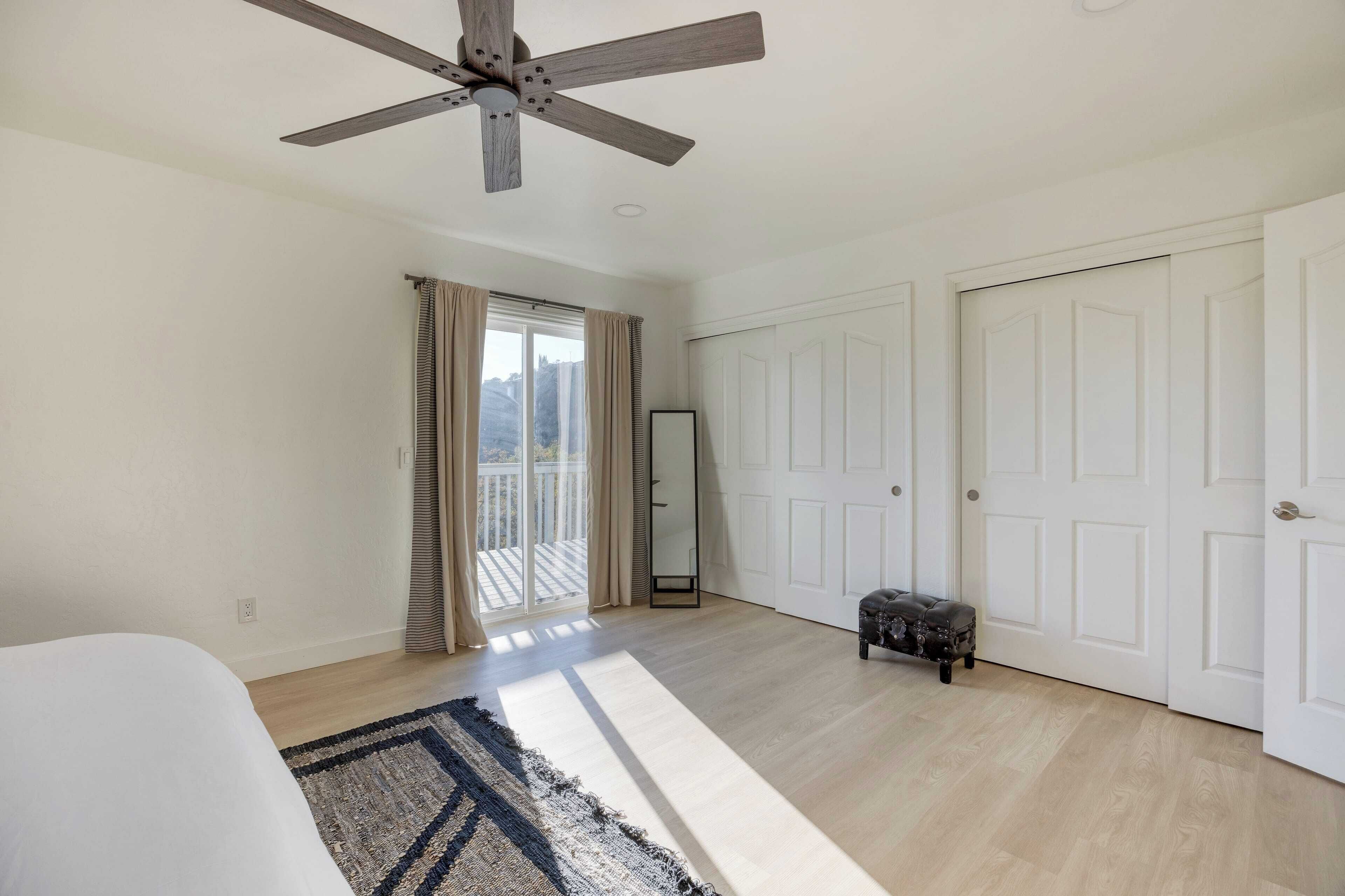 A spacious room with a ceiling fan, a large mirror, and a sliding glass door leading to an outdoor area.