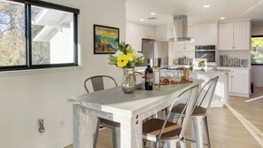 Una cocina moderna con armarios blancos, una isla central y una zona de comedor con una mesa rústica.