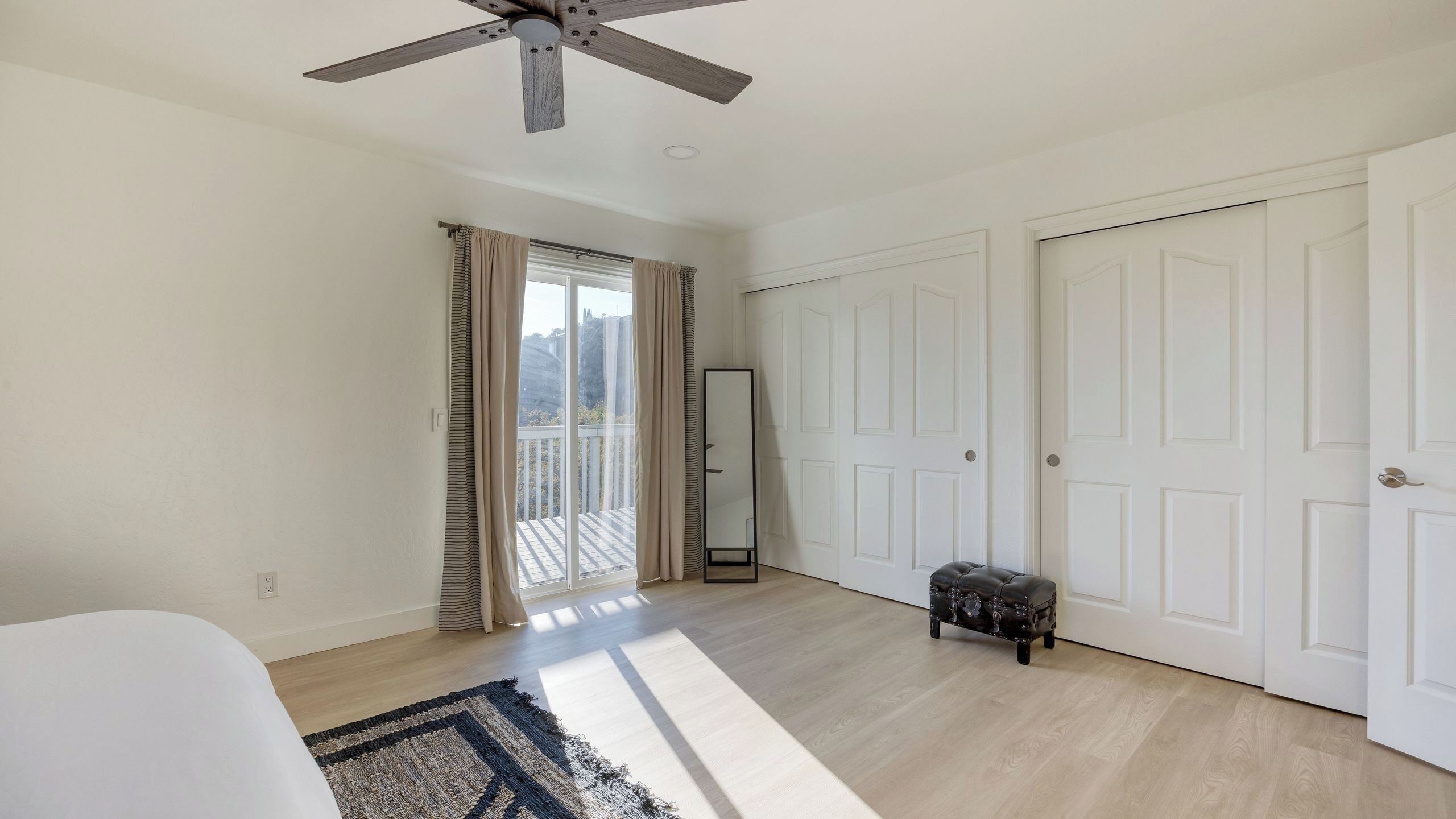 A room with a ceiling fan, a large mirror, a bench, and a view through a window.
