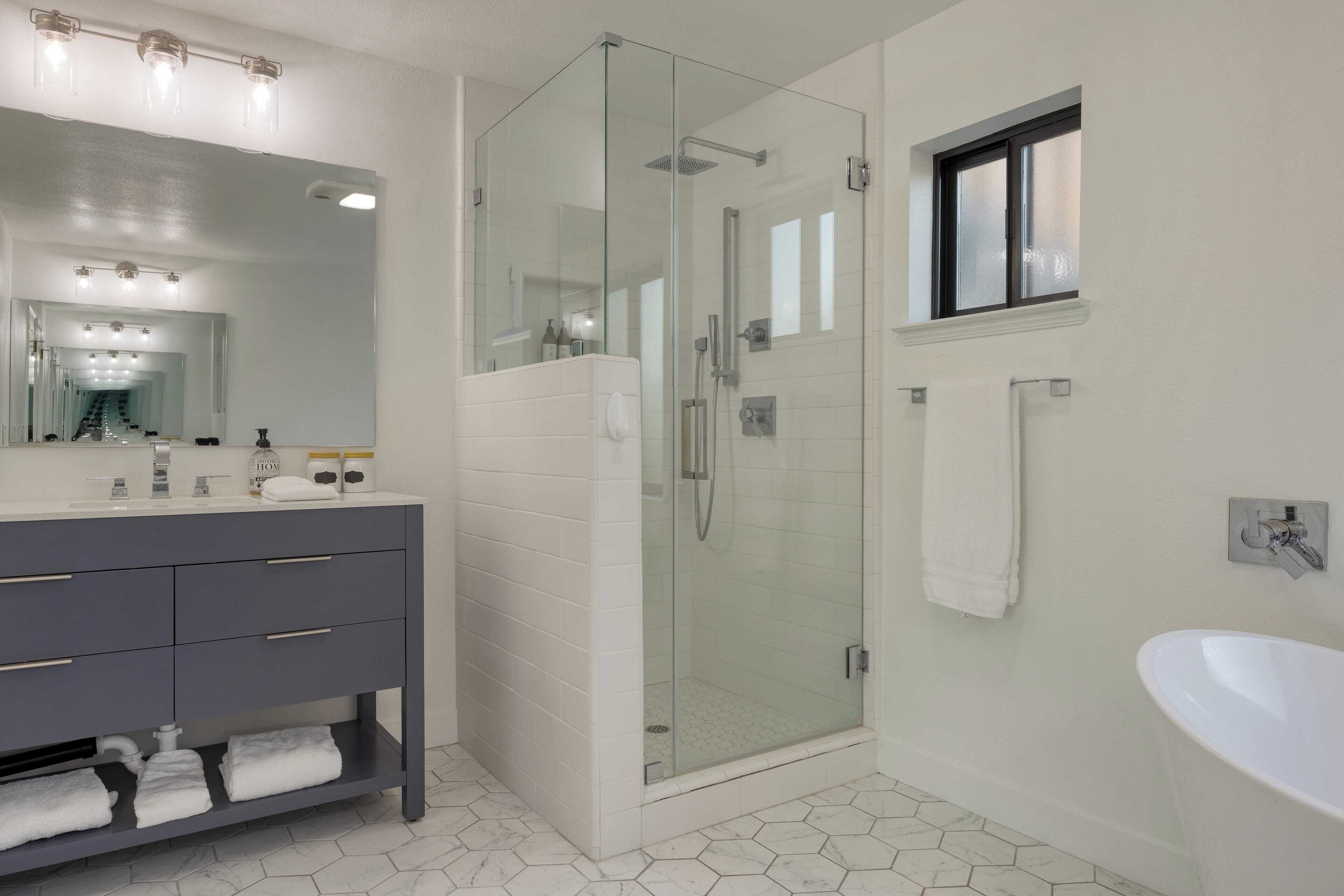 Un baño moderno con ducha de vidrio, un espejo grande y un lavamanos blanco.
