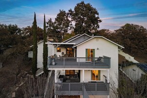 Una casa de dos pisos con balcón, una escalera y vista a árboles.