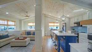 Une cuisine moderne dotée d’un îlot central, d’un plafond en bois et de grandes fenêtres.
