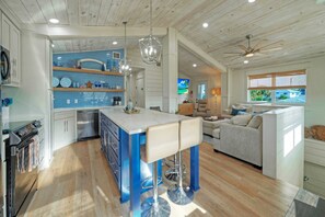 Een moderne keuken met blauwe kastjes, een centraal kookeiland met barkrukken, roestvrijstalen apparatuur en een plafondventilator.