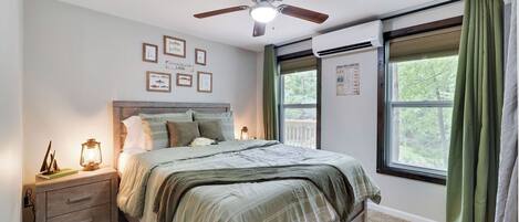 A bedroom with a bed, a nightstand, a ceiling fan, a window with curtains, and wall decorations.