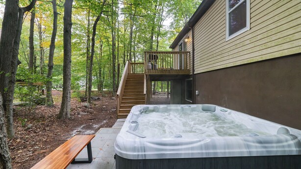 Ein Whirlpool inmitten von Bäumen mit einer Holzdar Terrasse und einer Treppe, die zu einem Haus führt.