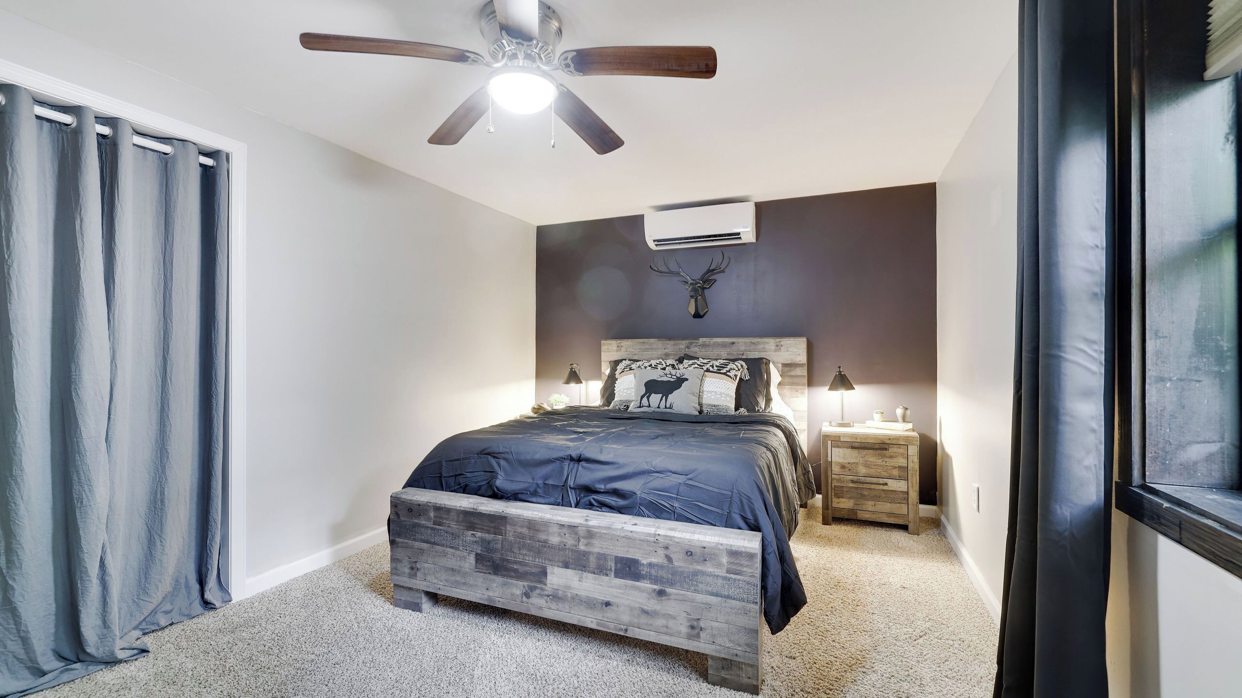Un dormitorio con cama, ventilador de techo, aire acondicionado, mesita de noche y ventana.