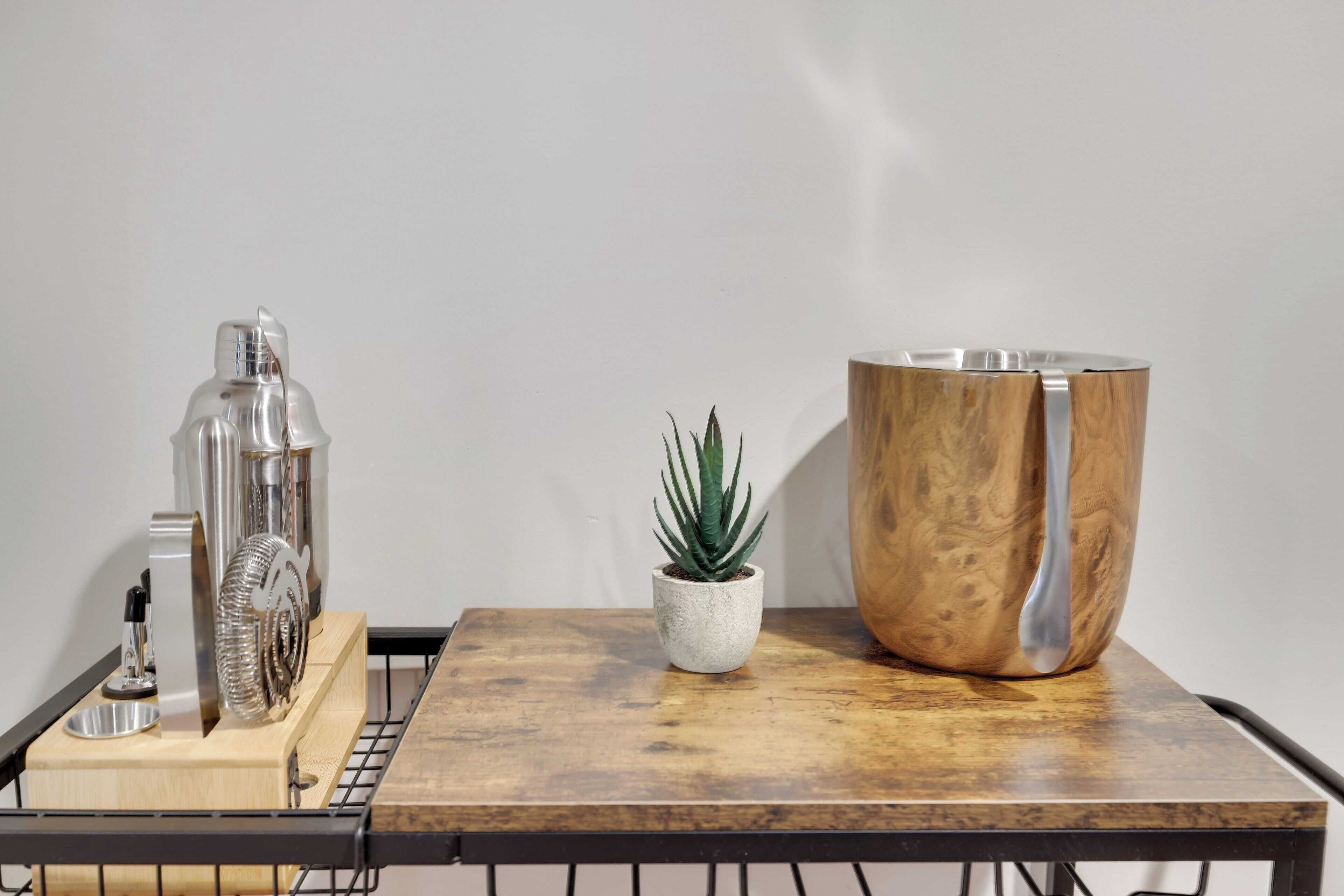 A wooden table with a metal bottle, a small potted plant, and a wooden bowl.