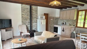 A cozy living room with a sofa, a TV, and a fireplace. Adjacent is a kitchen with a stove, oven, and sink. - Charming Périgord house with above-ground pool (Mauzac-et-Grand-Castang)