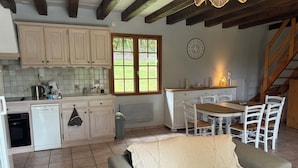 A kitchen with white cabinets, a dishwasher, a sink, and a window with a view of greenery. There is a dining table with chairs and a clock on the wall. - Charming Périgord house with above-ground pool (Mauzac-et-Grand-Castang)