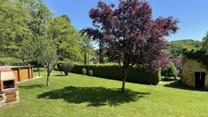 A well-maintained lawn with a wooden barbecue area and a stone building in the background. - Charming Périgord house with above-ground pool (Mauzac-et-Grand-Castang)