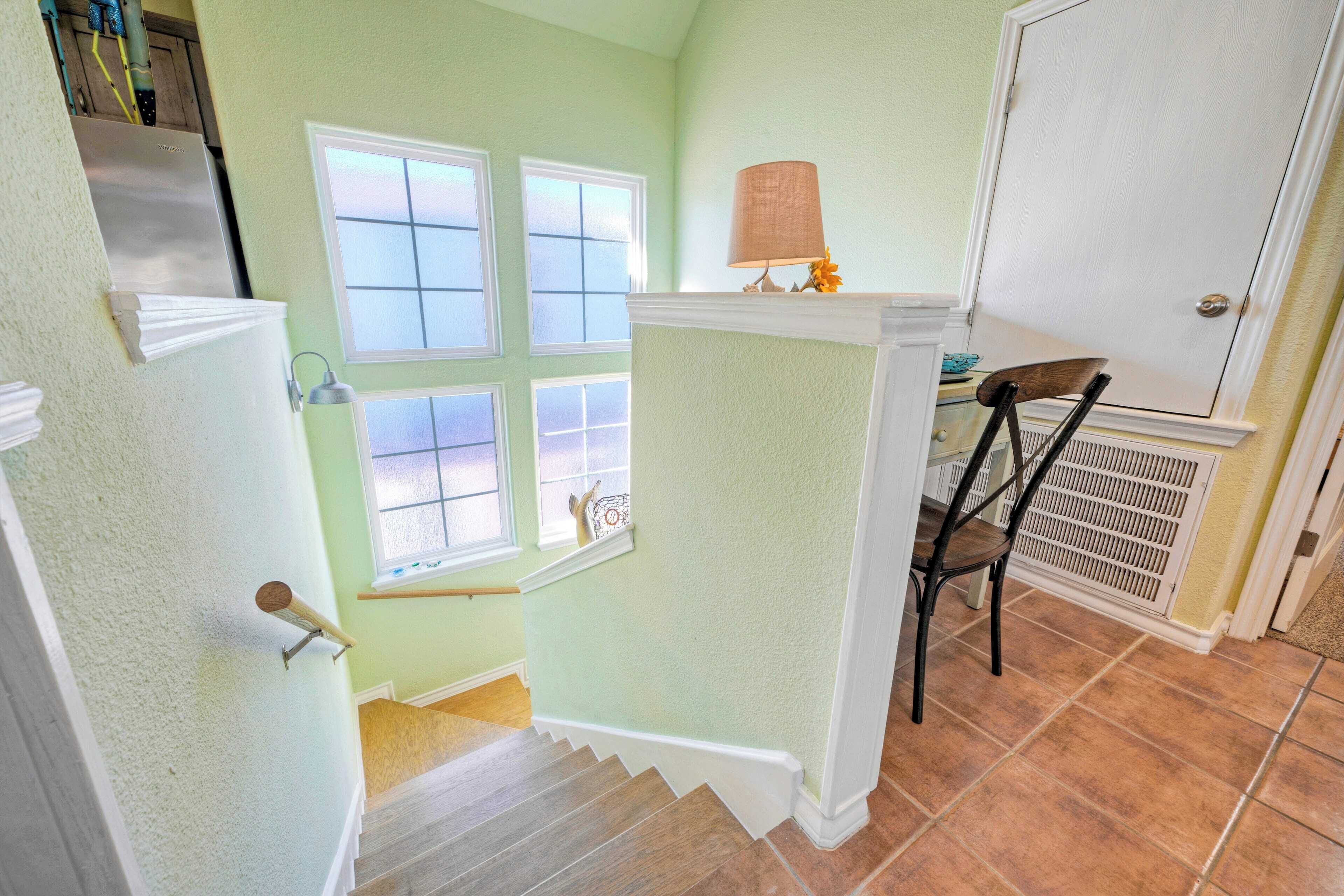 A stairway with a white handrail, a window with a view, and a chair near a door.