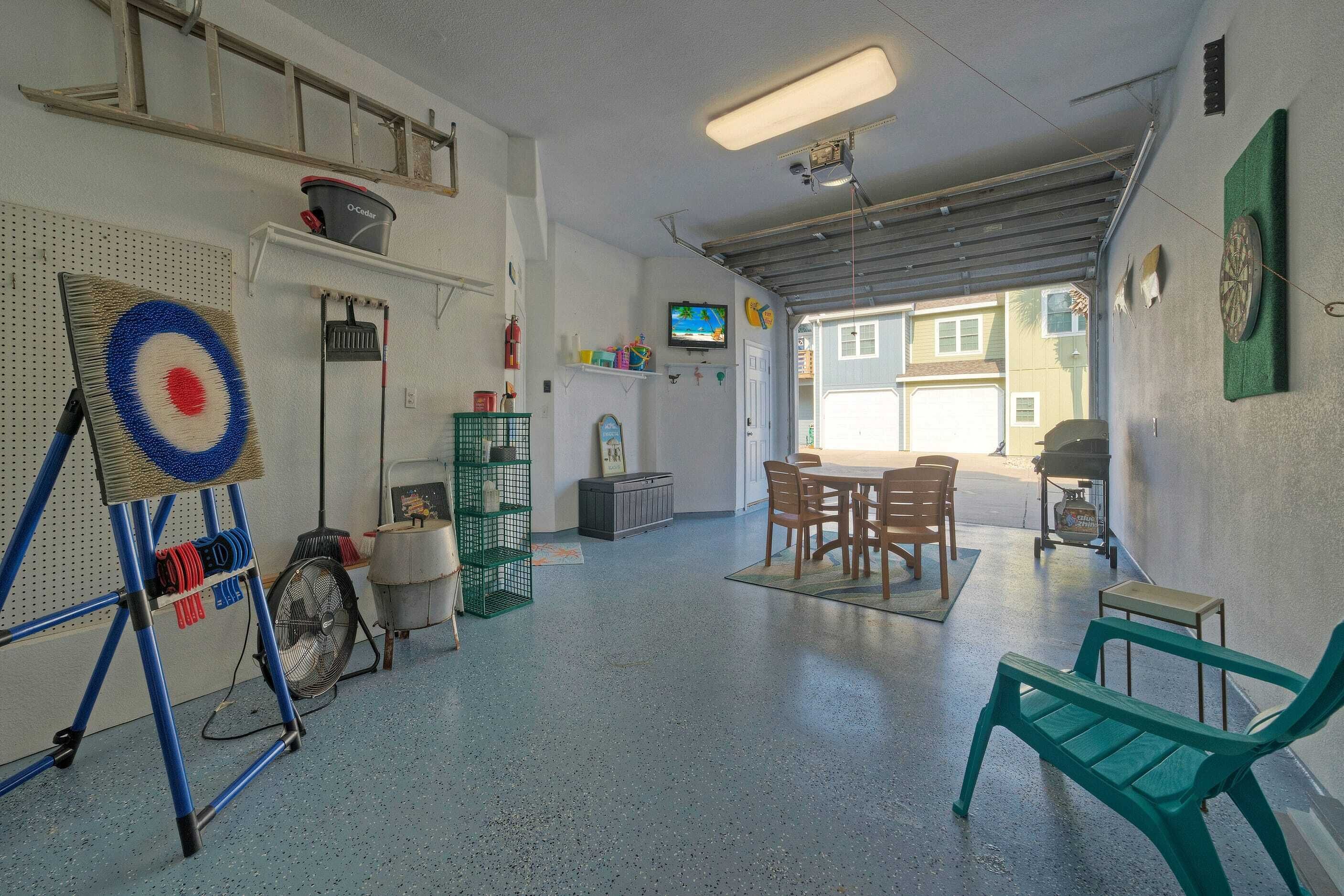 Un garatge amb un objectiu al mur, un ventilador, una taula amb cadires i una banca verda.