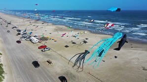 A beach with numerous kites, a parking area, and a view of the ocean. - Communal Pool, Beach Gear & Prime Location Near Port Aransas Beaches Salty Seas by Avantstay (Port Aransas)