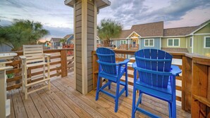 A wooden deck with two blue Adirondack chairs, a wooden table, and a view of houses in the background. - Communal Pool, Beach Gear & Prime Location Near Port Aransas Beaches Salty Seas by Avantstay (Port Aransas)