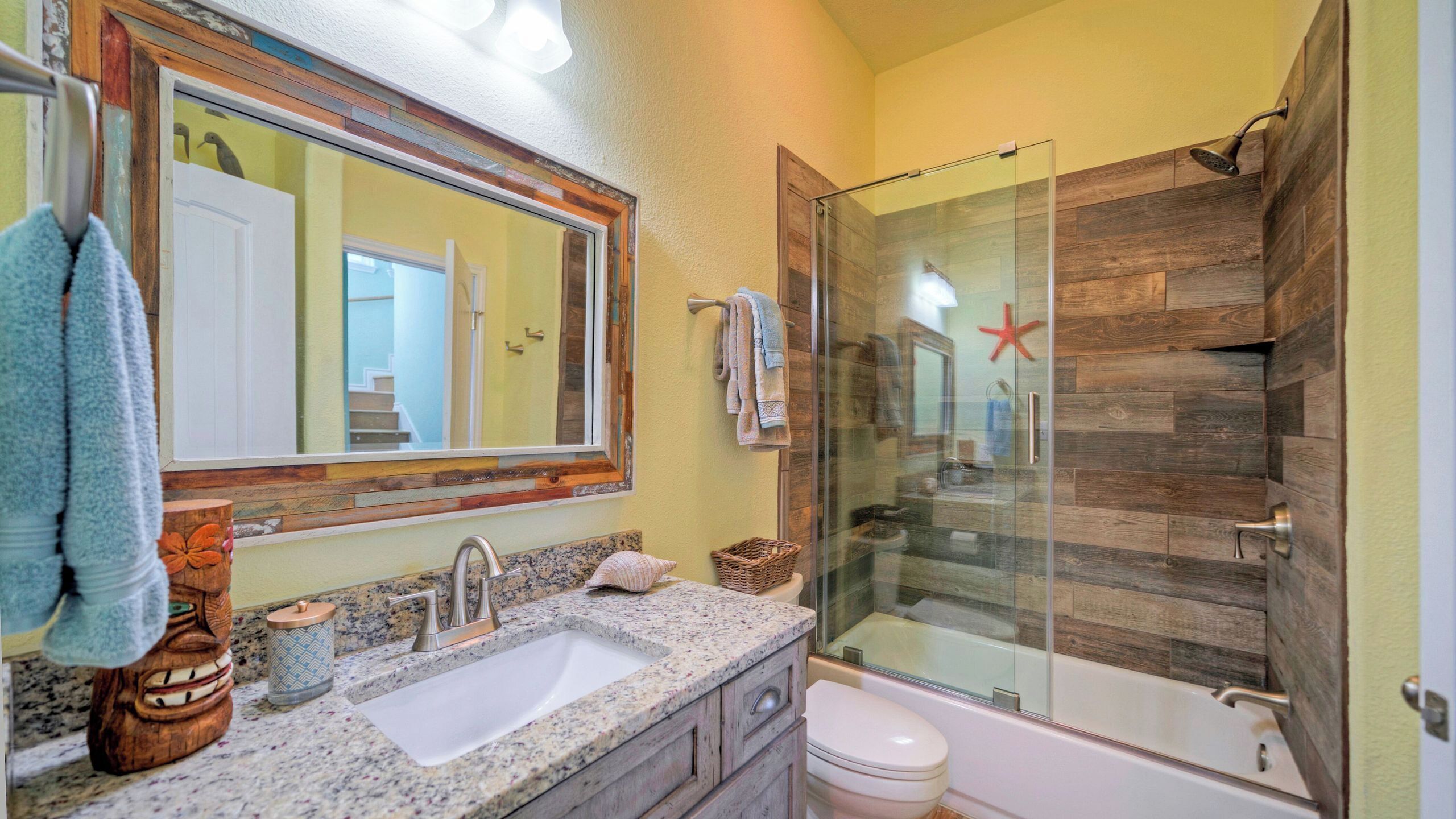 A bathroom with a glass shower enclosure, a sink with a granite countertop, and a toilet.