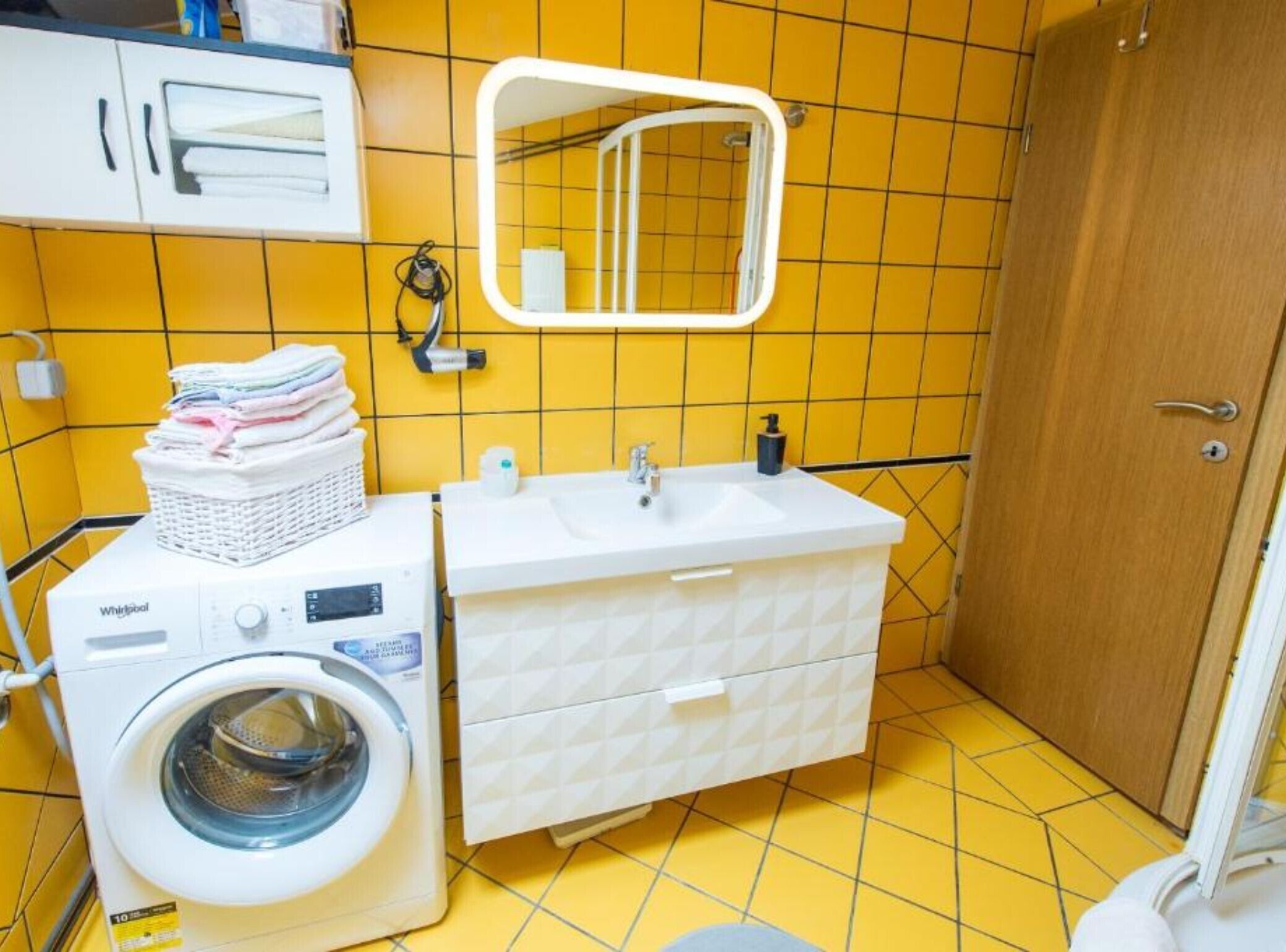 Een kleine badkamer met een wasmachine, een wastafel en een spiegel.