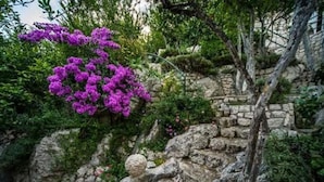 Un muro de piedra con un árbol y flores moradas.
