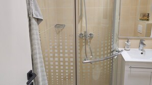 A glass-enclosed shower with a handheld showerhead and a handheld shower attachment.