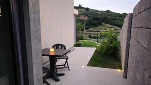 An outdoor patio with a table and chairs, a candle, and a view of a vineyard.