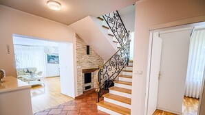 A spacious living area with a fireplace, a staircase with ornate metal railings, and a kitchen area. - Stunning Rural Holiday Home with Garden and BBQ - Four Bedroom Holiday Home (Brežice)
