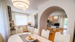 A modern living room with a dining area, featuring a large table, white sofas, and a kitchen in the background. - Stunning Rural Holiday Home with Garden and BBQ - Four Bedroom Holiday Home (Brežice)