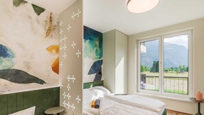 A modern bedroom with a large bed, a view of mountains, and a green accent wall.