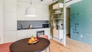 A modern kitchen with white cabinets, a black countertop, and a round dining table with a fruit bowl.