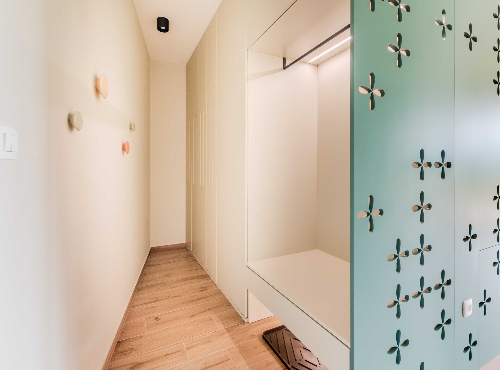 Un couloir d’hôtel moderne avec un revêtement de sol en bois, un design minimaliste et un mur végétal agrémenté de motifs décoratifs.