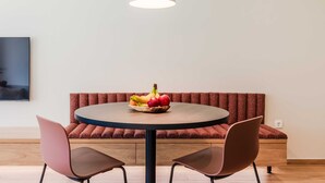A dining area with a round table, two chairs, a bench, and a hanging light fixture.