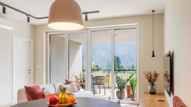 A modern living room with a round table, a sofa, and a balcony with a mountain view.