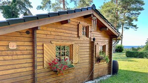 A wooden cabin with a sloped roof, a small porch, and a window with a flower box. - Almhuetten-am-Meer.de (Lubmin)