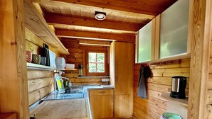 A compact kitchen with wooden walls, a granite countertop, and a window providing natural light. - Almhuetten-am-Meer.de (Lubmin)