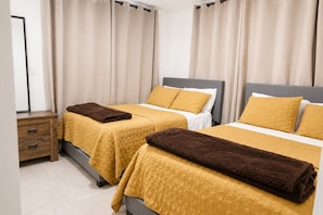 Ein Doppelzimmer mit zwei Betten, jeweils mit Daunendecke und Kissen, einem Nachttisch und einem Spiegel.