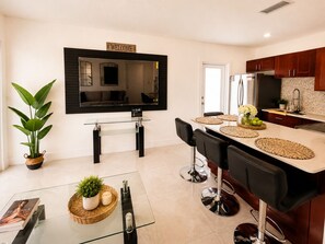 A modern kitchen with a TV, bar area, and a dining table with chairs.