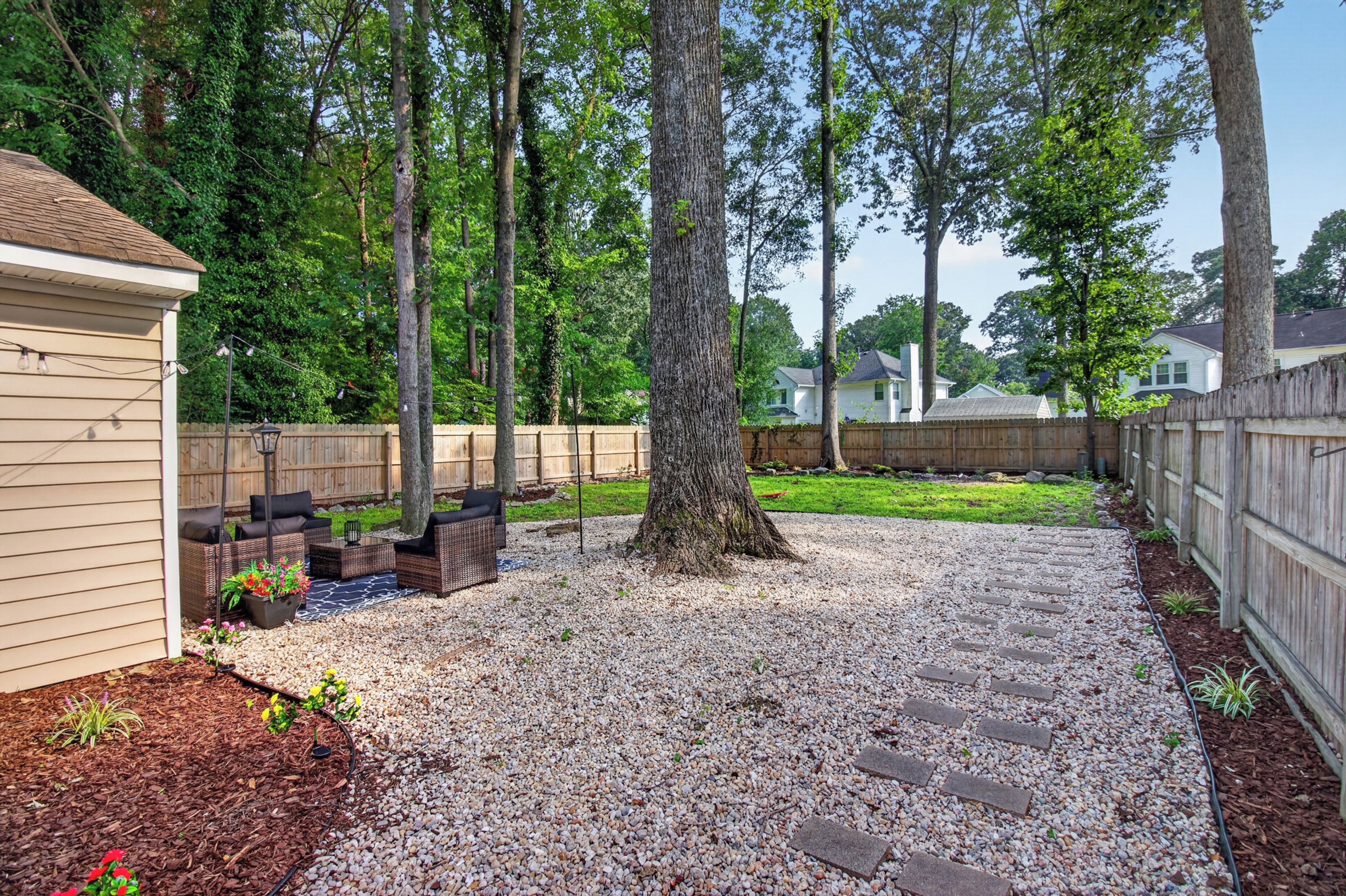 Un jardin avec un espace patio, une clôture en bois et une pelouse.