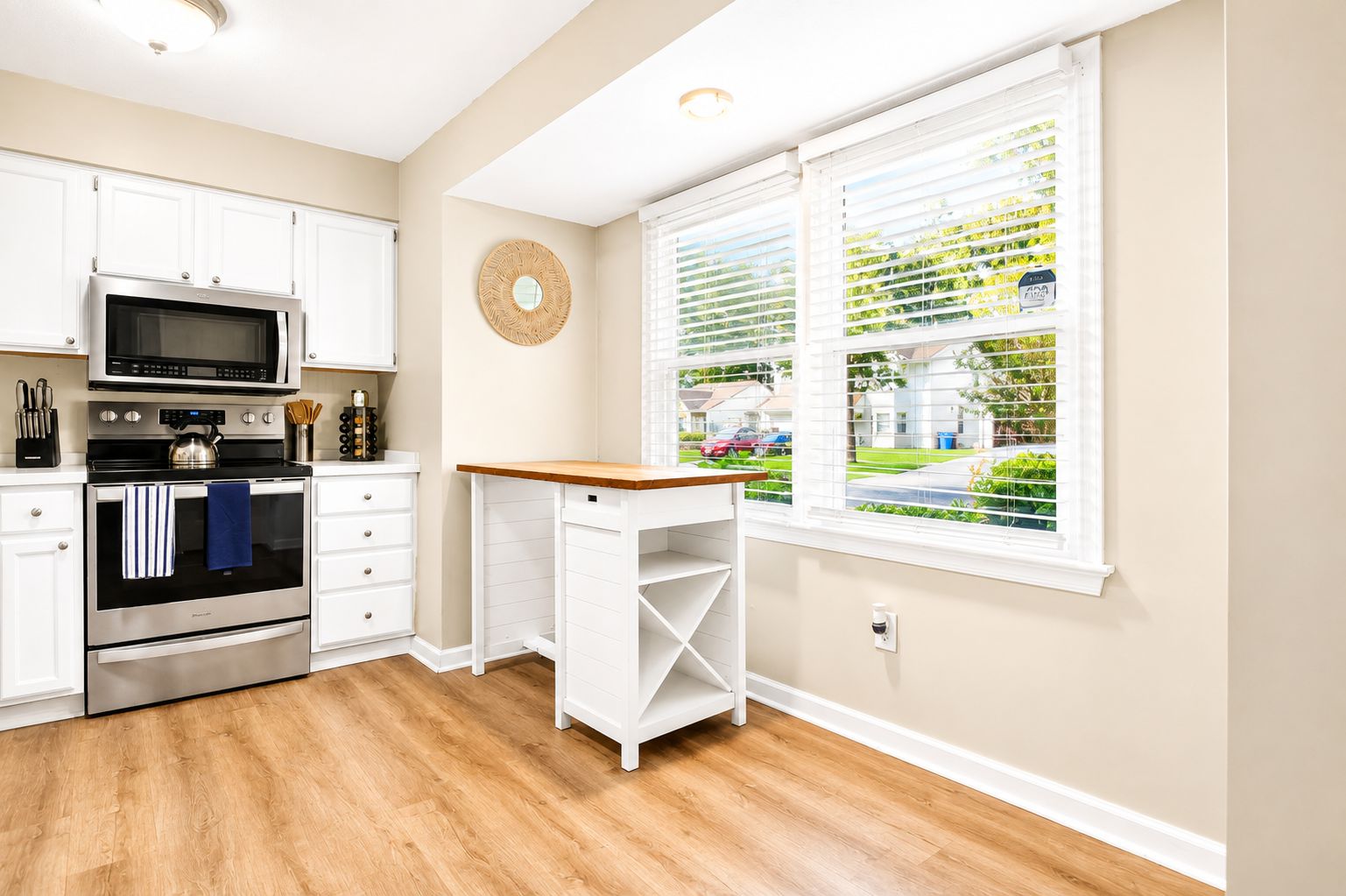 A kitchen with white cabinets, a microwave, stove, and a window with blinds.