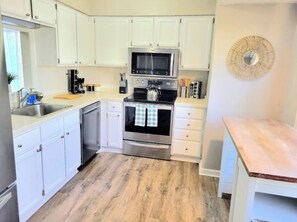 Kitchen features a microwave, oven, and dishwasher, along with a wooden countertop and woven wall decoration.