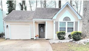 Stylish single-story home with a gabled roof and central entrance door, set amidst a well-manicured lawn and trees.