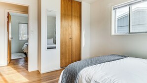 Un dormitorio con un armario de madera, una cama con edredón gris y blanco, y una ventana con persianas.