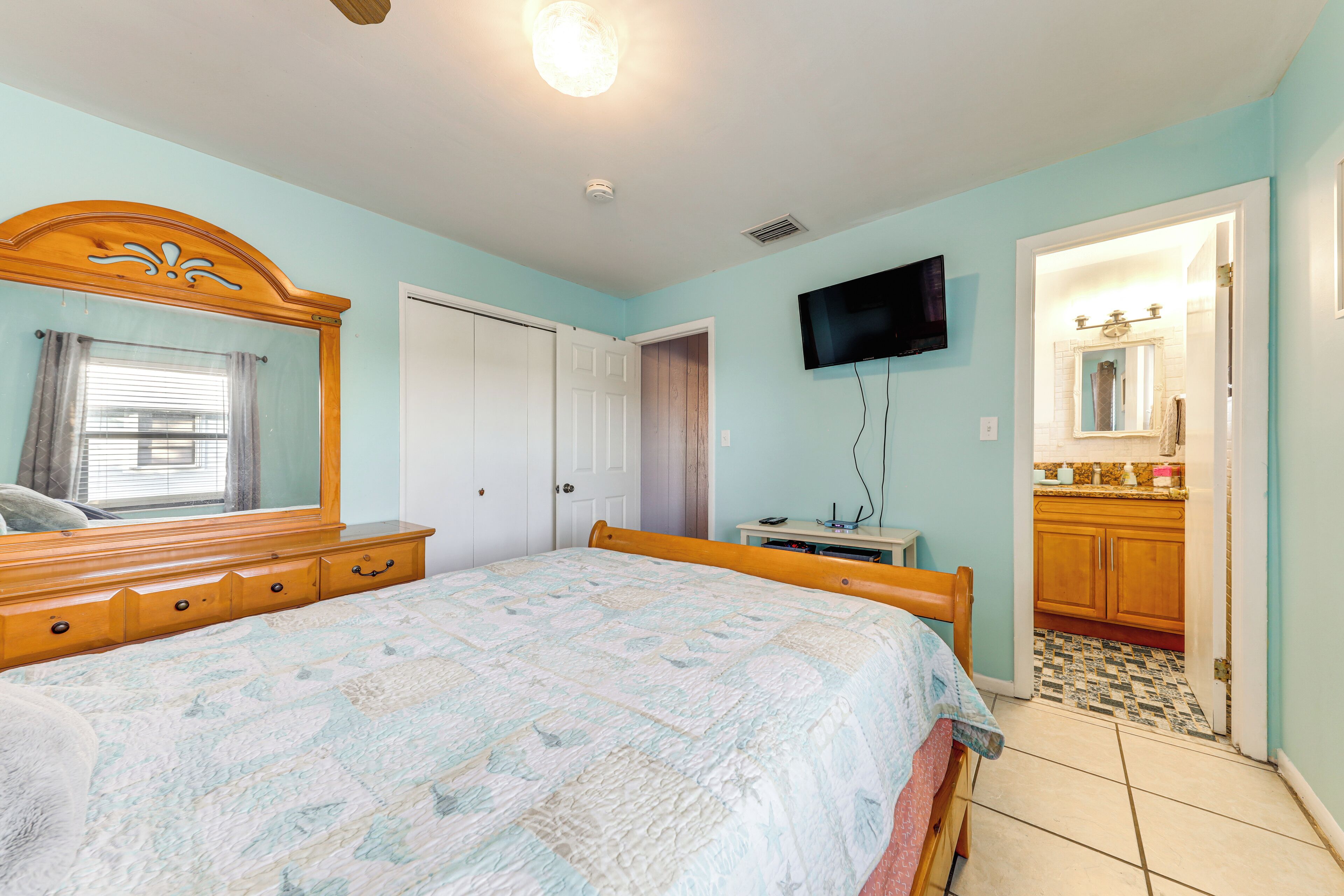 Un dormitorio con cama, cómoda, televisor y baño a la vista a través de una puerta abierta.