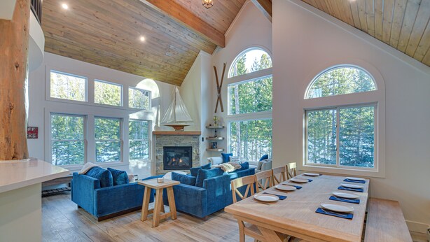 A spacious living room with a fireplace, large windows, and a dining area with wooden furniture. - Mtn Escape w/ Hot Tub, By Trails in Grand Lake! (Grand Lake)